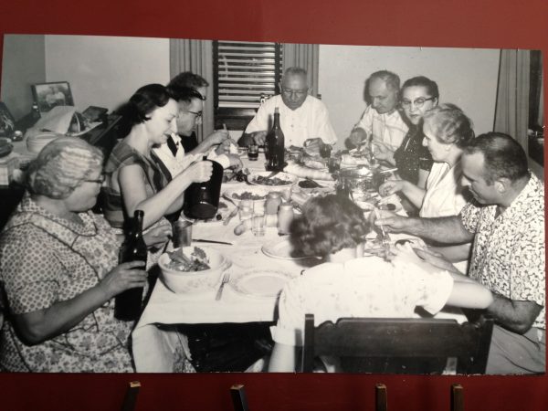 An extended family eating a meal with bottles of wine and plates of food all around